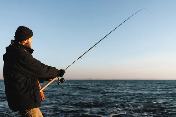 Silhouette of man fisherman wearing coat, holding rod