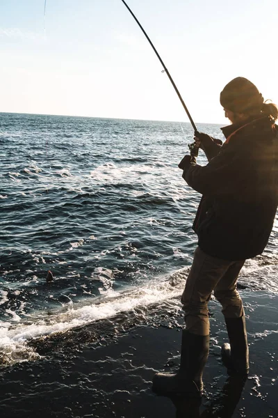 Silhouette dell'uomo pescatore che indossa cappotto, asta di tenuta — Foto Stock