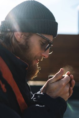 Sahilde sıcak çay içen palto ve şapka giyen yakışıklı genç adam balıkçı.