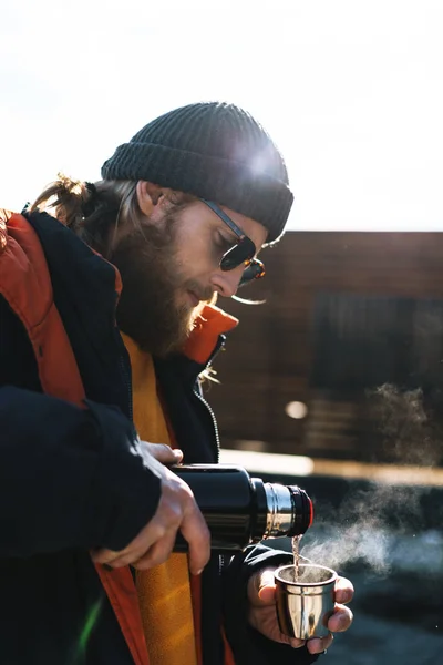 Красивый молодой человек рыбак в пальто и шляпе на берегу моря пьет горячий чай . — стоковое фото