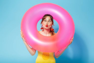 Mayo giymiş genç bir kız şişirilebilir halkada mavi arka planda yalnız poz veriyor..