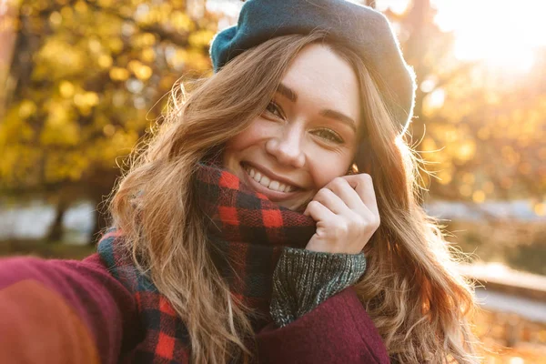 Beautiful happy young pretty woman walking outdoors in autumn spring park take a selfie by camera. — Stock Photo, Image