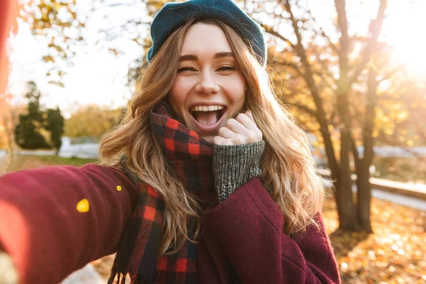 Beautiful happy young pretty woman walking outdoors in autumn spring park take a selfie by camera. — Stock Photo, Image