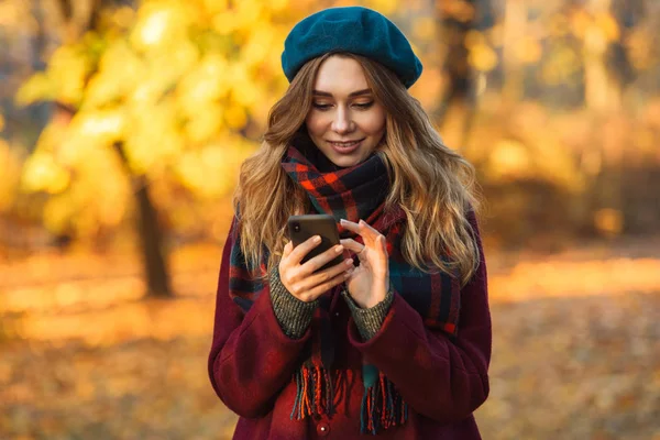 携帯電話のチャットを使用して秋の春の公園で屋外を歩く幸せな若いかわいい女性. — ストック写真