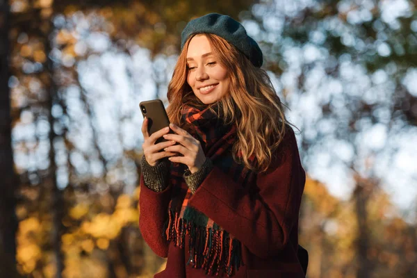 Mutlu genç güzel kadın cep telefonu sohbet kullanarak sonbahar bahar parkı açık havada yürüyüş. — Stok fotoğraf