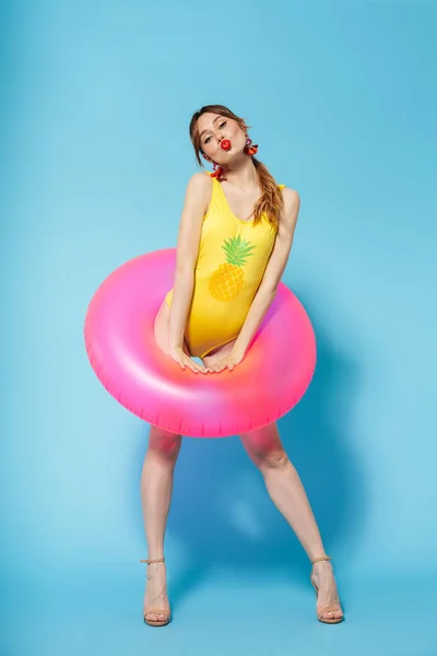 Young pin up pretty summer girl in swimwear posing isolated over blue background in inflatable ring. — 스톡 사진