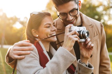 Sonbahar parkında yürürken retro kamera fotoğraf çeken gülümseyen çift portresi