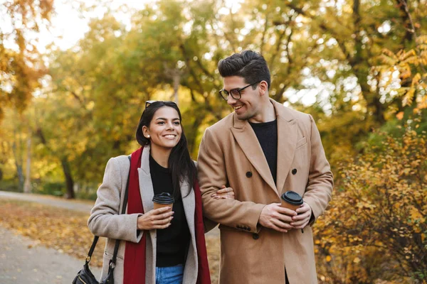 Porträt eines europäischen Paares, das beim Spazierengehen im Herbstpark Kaffee zum Mitnehmen aus Pappbechern trinkt — Stockfoto