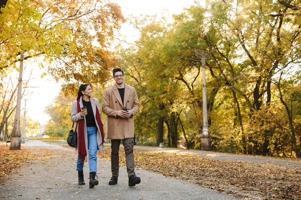 Porträt eines jungen Paares, das im Herbstpark Kaffee zum Mitnehmen aus Pappbechern trinkt — Stockfoto