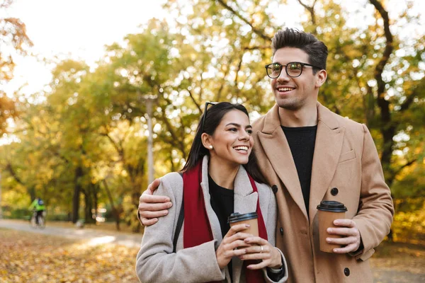 Retrato de pareja caucásica tomando café para llevar de vasos de papel mientras camina en el parque de otoño —  Fotos de Stock