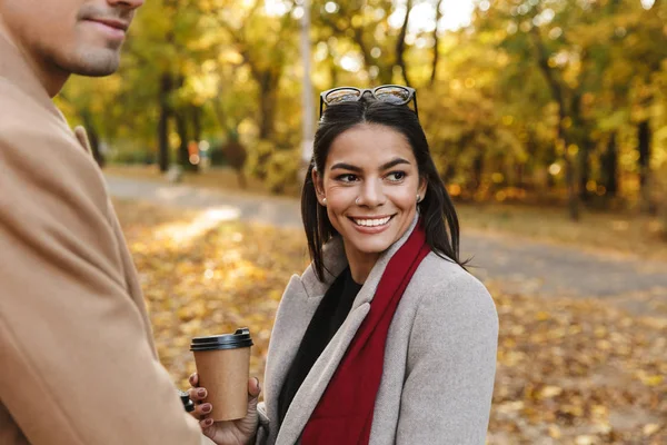 Retrato de mulher jovem casual com seu namorado bebendo café takeaway e sorrindo no parque de outono — Fotografia de Stock