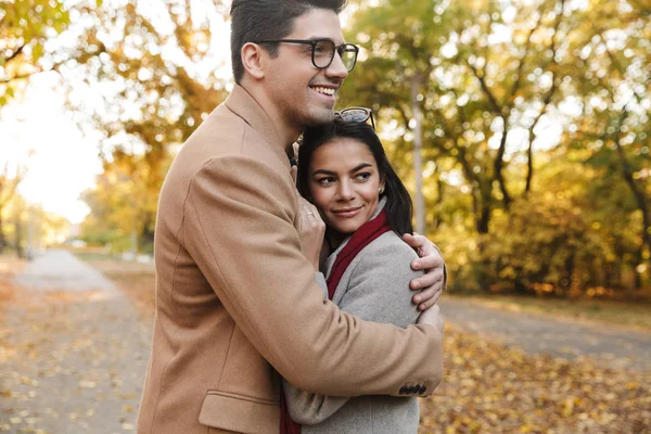 Imagen de la joven pareja morena sonriendo y abrazándose en el parque de otoño —  Fotos de Stock