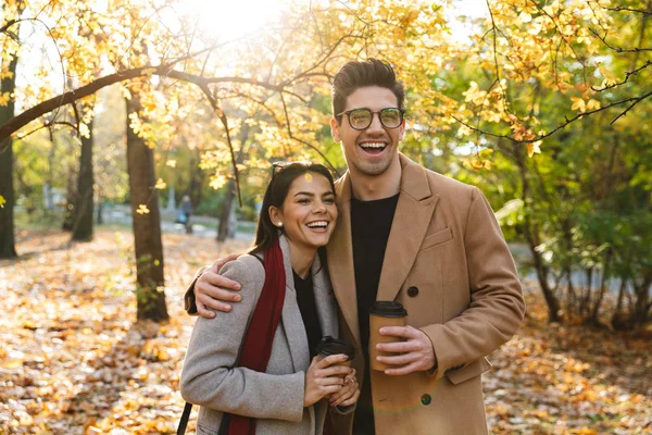 Retrato de pareja riendo hombre y mujer tomando café para llevar mientras caminan en el parque de otoño —  Fotos de Stock