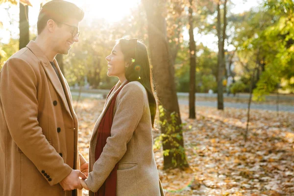 秋の公園で笑顔と手をつないでいる若い楽しいカップルのイメージ — ストック写真