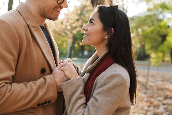 Imaginea unui cuplu tânăr zâmbitor care se ține de mână și se uită unul la celălalt în parcul de toamnă — Fotografie, imagine de stoc