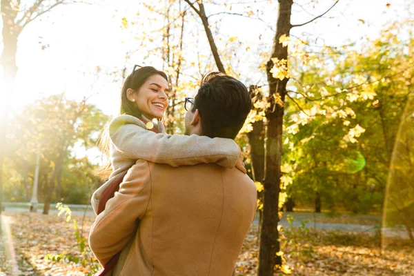 Изображение европейского мужчины, несущего улыбающуюся женщину в руках осенью — стоковое фото