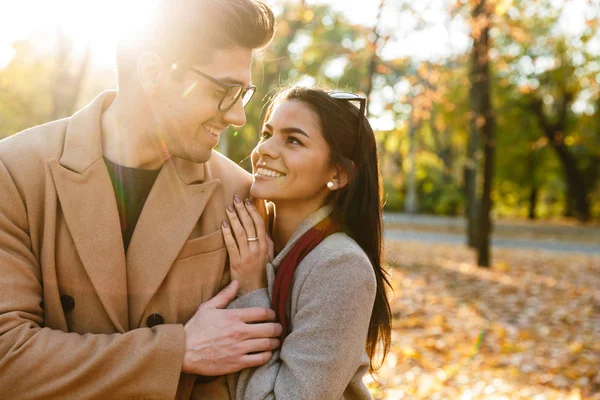 Imagine de brunetă cuplu caucazian zâmbind și îmbrățișându-se în parcul de toamnă — Fotografie, imagine de stoc