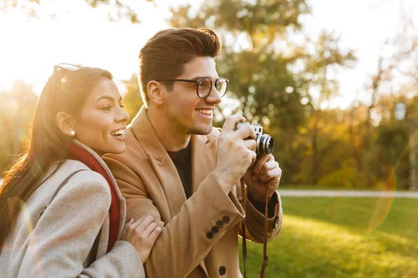 Retrato de pareja casual tomando fotos en cámara retro y sonriendo mientras camina en el parque de otoño —  Fotos de Stock