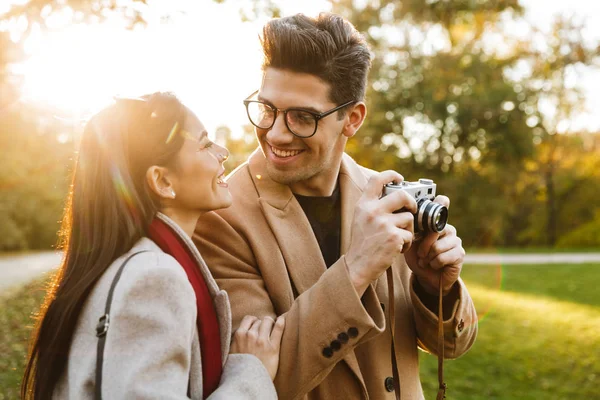 Retrato de pareja feliz usando cámara retro y mirándose mientras caminan en el parque de otoño —  Fotos de Stock