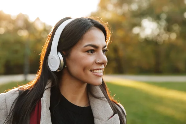 Porträtt av lycklig vacker kvinna klädd i päls Lyssna på musik med hörlurar och leende i parken — Stockfoto