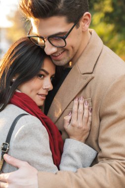 Sonbahar parkında yürürken birbirlerine gülümseyen ve sarılan sıradan romantik çiftin portresi