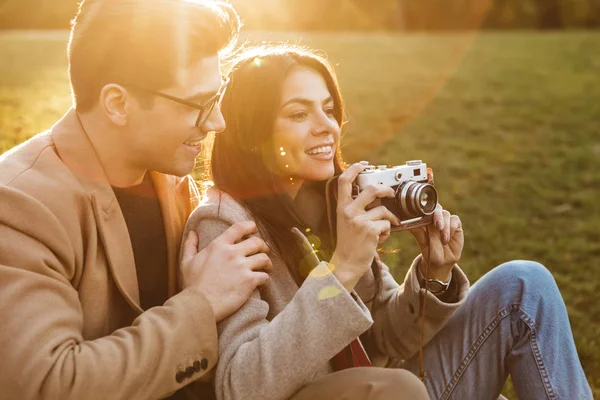 随意夫妇的肖像在复古相机上拍照，坐在公园的草地上微笑 — 图库照片
