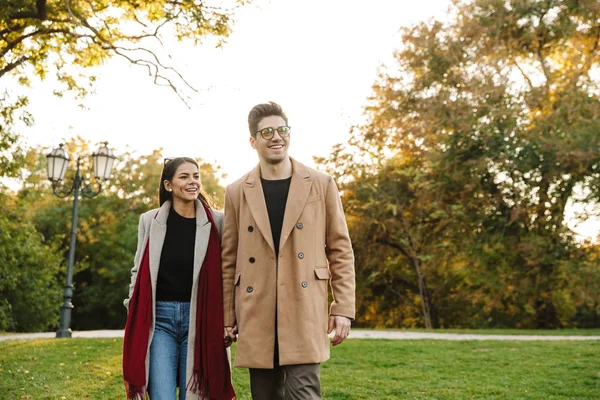 Retrato de pareja casual joven sonriendo a la cámara y caminando en el parque de otoño —  Fotos de Stock