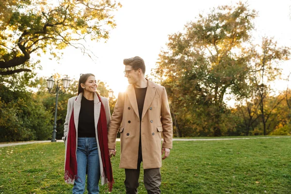 Retrato de pareja casual sonriente mirándose y caminando en el parque de otoño —  Fotos de Stock