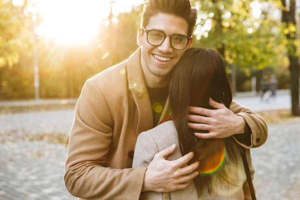 Image of brunette handsome man hugging his girlfriend and smiling in park — Stock Photo, Image