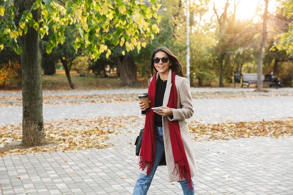 Portrait of nice casual woman wearing sunglasses drinking takeaway coffee and using cellphone n autumn park — Stock Photo, Image