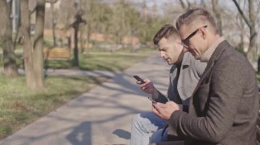 Parkta otururken konuşan ve gülen akıllı telefonlar ile iki güzel yetişkin erkek
