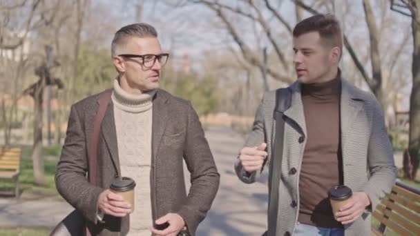 Dois Homens Adultos Bonitos Com Xícaras Café Conversando Enquanto Caminham — Vídeo de Stock