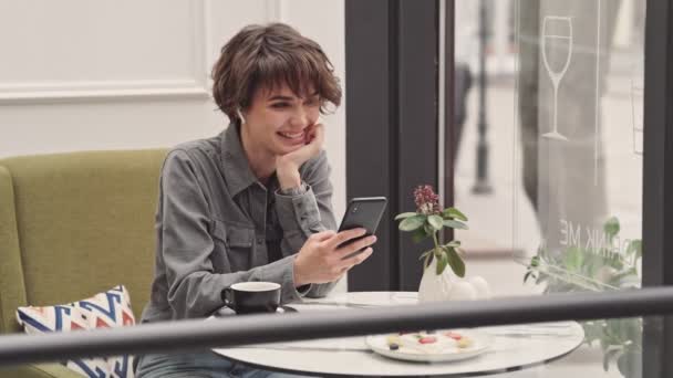 カフェに座ってスマートフォンでビデオ通話を持つかなり若い女性 — ストック動画