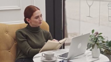 Kafede oturan kitap okuyan pensive genç kadın