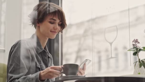 Través Vista Ventana Joven Sonriente Charlando Teléfono Inteligente Sentado Café — Vídeos de Stock