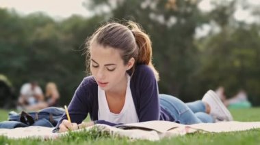 Gülümseyen esmer kadın çim üzerinde yatan ve parkta dizüstü bir şey yazma