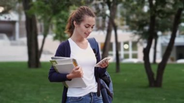 Parkta akıllı telefon kullanarak sırt çantası ve kitap ile Mutlu esmer kadın