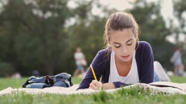 Joven Morena Tumbada Hierba Escribiendo Algo Cuaderno Mientras Bosteza Parque — Vídeo de stock