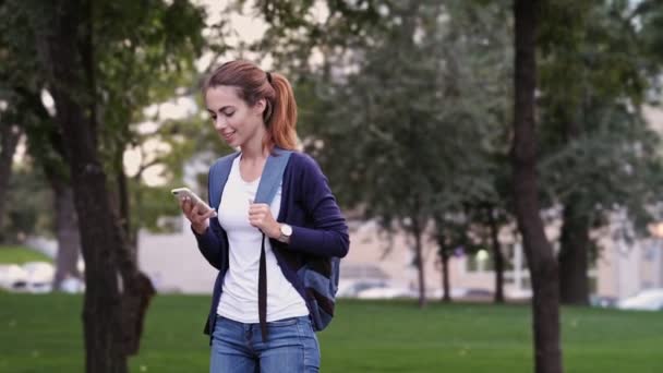 Glückliche Brünette Frau Mit Rucksack Mit Ihrem Smartphone Park — Stockvideo