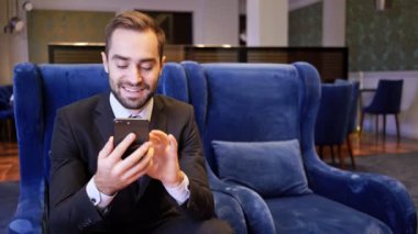Kafede koltukta otururken akıllı telefon kullanan mutlu sakallı iş adamı