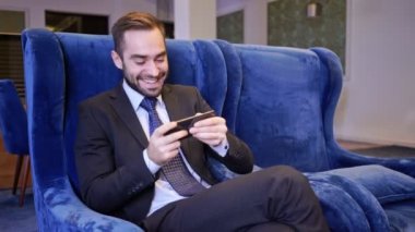 Kafede koltukta otururken akıllı telefonda oynayan mutlu sakallı iş adamı