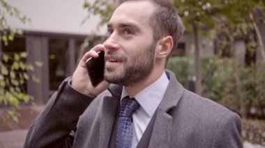 Şehirde açık havada dururken akıllı telefon ile konuşan palto mutlu yakışıklı iş adamı