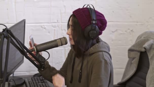 ラジオで放送中にスマートフォンを使って帽子をかぶったハッピー可愛いDj女性のサイドビュー — ストック動画