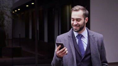 Şehirde açık havada yürürken akıllı telefon kullanarak ceket Mutlu yakışıklı iş adamı