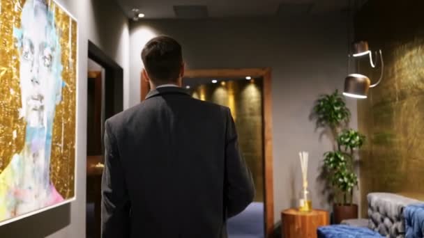 酷商人穿着外套的后视图 带着笔记本电脑穿过酒店走廊 — 图库视频影像