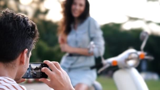 男は携帯電話でスクーターで屋外で彼のガールフレンドの写真を撮ります — ストック動画