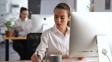 Genç güzel ciddi kadın pc bilgisayar yazma notları kullanarak ofiste çalışan