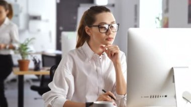 Genç güzel ciddi kadın pc bilgisayar kullanarak ofiste çalışan