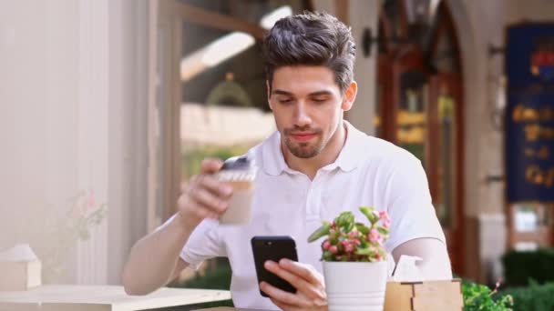 年轻的快乐帅哥坐在咖啡馆户外在街上用手机喝咖啡 — 图库视频影像