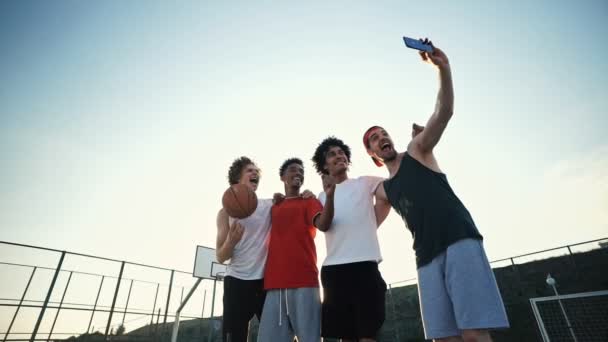 遊び場ながらスマートフォンで一緒に自分撮りを作る4人の多民族の友人を幸せに — ストック動画